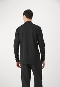 Zwarte longsleeve shirt met hoge kraag en een aansluitend ontwerp. Zacht materiaal met minimale naden, gedragen met bijpassende zwarte broek.