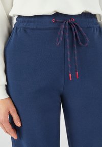 Navyblauwe broek met een gestructureerd oppervlak, voorzien van een elastische tailleband en een trekkoord met rode accenten.