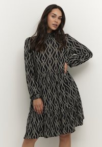 Robe noire avec un motif en forme de diamant blanc, dotée de longues manches, d'un col haut et d'une silhouette évasée arrivant au genou.