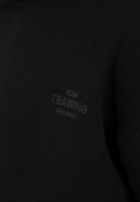 Zwarte sweatshirt met een zachte textuur met een vervaagd logo "TEAM TRAINING SMILODOX" aan de linkerkant gedrukt. Eenvoudig ontwerp, geen aanvullende details.