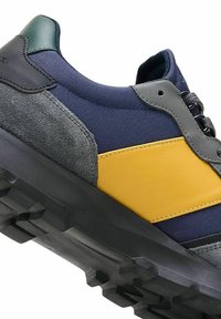 Zapatillas de hombre con textil azul marino, acentos de ante gris y una franja amarilla. Presentan una suela de goma negra texturizada y una lengüeta de talón verde.