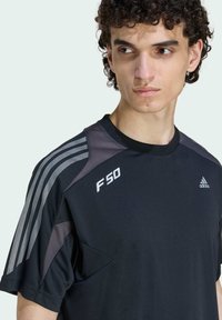 Crna atletska majica kratkih rukava, sivi detalji i tri bijele pruge na ramenu. Išiveni "F50" i logo sprijeda.
