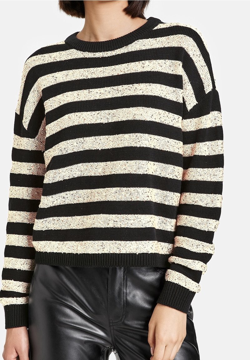 Gestreifter Pullover in Schwarz und Creme mit Rundhalsausschnitt und langen Ärmeln, ausgestattet mit einem strukturierten Strick und geripptem Saum. Kombiniert mit schwarzen Kunstlederhosen.