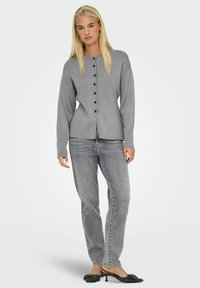 Grå kofta med rund halsringning, lång ärm och knappstängning fram. I kombination med ljusgrå jeans och svarta klackskor.