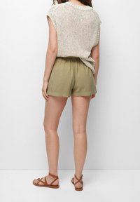 Khaki korte broek met een elastische tailleband, gecombineerd met een licht, gebreid beige top. Draagt beige sandalen met banden.