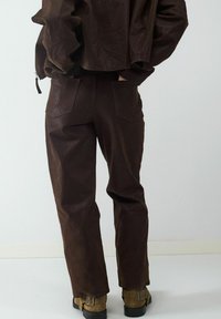 Bruine neplederen outfit met een cropped jack en bijpassende broek met een gladde textuur, zichtbare naden en twee achterkantzakken.