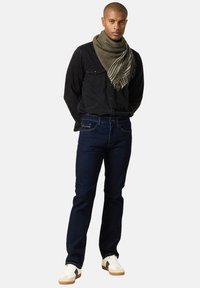 Jeans in denim scuro abbinati a una camicia nera con bottoni. Una sciarpa grigia con strisce bianche avvolge il collo. Sneakers bianche completano il look.