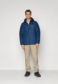 Navy blue puffer jacket with horizontal quilting and zippered front, paired with light beige cargo pants and black shoes.