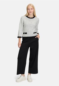 Weißer strukturierten Pullover mit schwarzem Rand und Taschen, kombiniert mit schwarzen weit geschnittenen Hosen und weißen Turnschuhen. Lässiges Outfit mit kontrastierenden Elementen.
