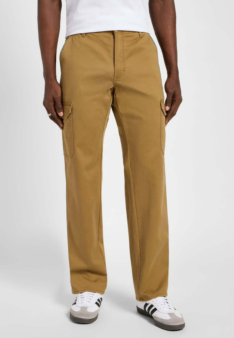 Pantaloni cargo color khaki con una vestibilità ampia, dotati di tasche laterali, fronte piatto e un tessuto liscio e resistente. Indossati con sneakers bianche e grigie.