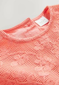 Top sans manches rose corail avec broderie florale en dentelle et superposition en tulle, avec un col rond et une étiquette de la marque NEXT à l'intérieur.
