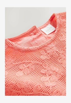 Koraljna čipkasta bluzica s cvjetnim vezom; ima okrugli izrez i teksturiranu tkaninu koja otkriva uzorak u obliku mreže. Vidljiva oznaka branda.