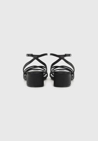 Sandales à talons noirs avec des brides croisées, un talon carré, et une texture lisse, comportant une fermeture par boucle simple à l'arrière.