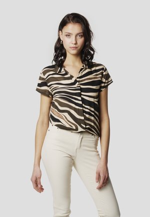 Camisa de manga corta con botones en beige con rayas de cebra en negro y marrón, con cuello y corte relajado, combinada con pantalones de color crema.