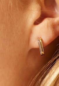 Gouden en zilveren dubbele oorring, met een gladde textuur en gepolijste afwerking, gemonteerd op een close-up van het oor.