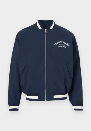 Μπλε ναυτικό μπουφάν bomber με φερμουάρ, με λευκές ρίγες στους μανσέτες και στο τελείωμα, με το κείμενο "Tommy Jeans Since 1985 New York City" στο αριστερό στήθος.