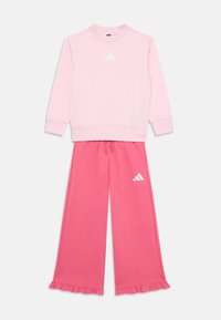 Sweatshirt rose avec logo blanc et manches longues, associé à un pantalon rose à jambes larges avec des poignets froncés et des détails de logo.