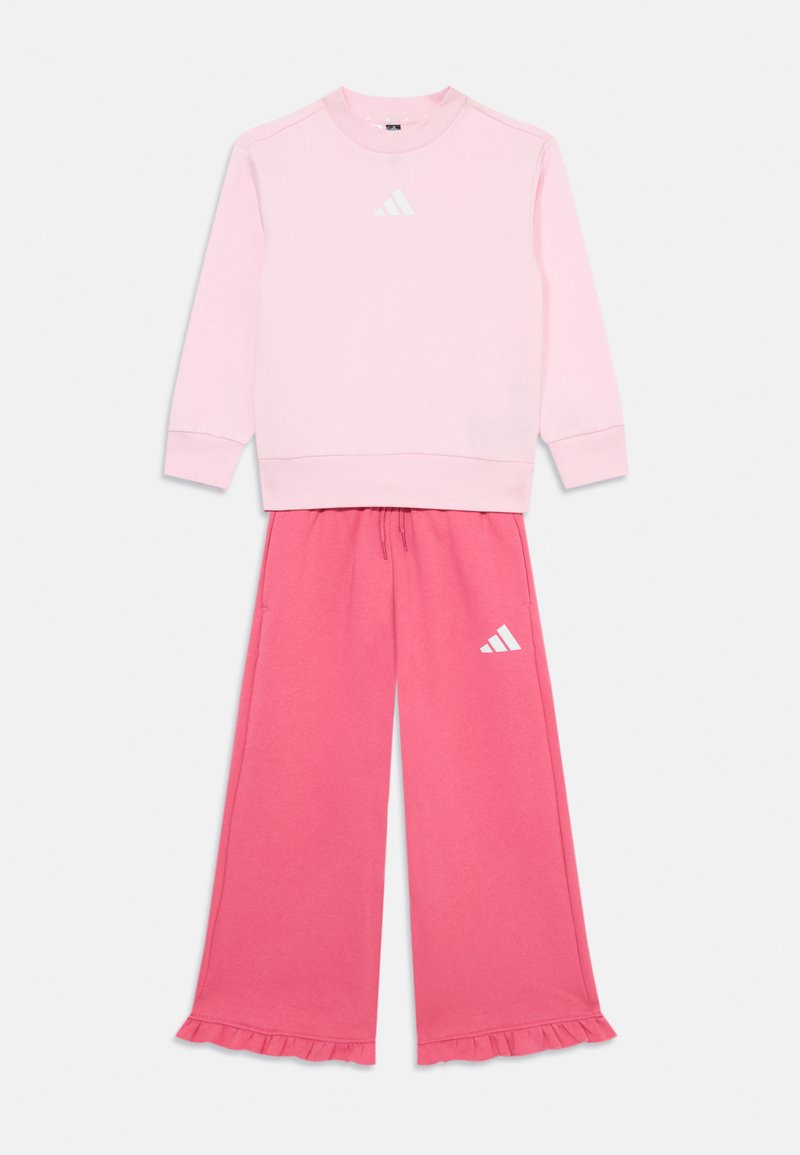 Sweatshirt rose avec logo blanc et manches longues, associé à un pantalon rose à jambes larges avec des poignets froncés et des détails de logo.
