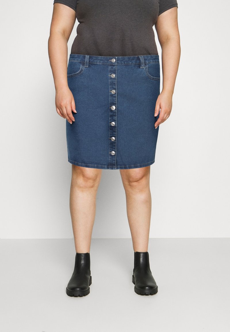 Jupe en denim avec une silhouette droite, couleur bleu foncé, cinq boutons sur le devant et poches latérales. Associée à des bottines noires.