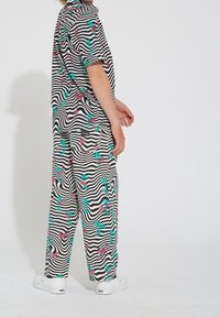 Tenue rayée noir et blanc ornée de flamants roses et de palmiers verts, fabriquée en tissu léger. Des chaussures blanches complètent le look.