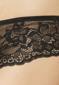 Svart blonde undertøy med intrikate blomster-detaljer, bølgete kanter og en myk, gjennomsiktig tekstur. Designet for en tett passform.