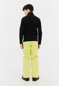 Czarny polar z wysokim kołnierzem, połączony z jasnobrązowymi wodoodpornymi spodniami i czarnymi butami, widok z tyłu.