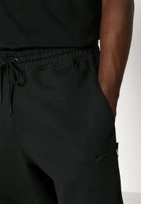 Czarne dresowe spodnie z elastycznym pasem w talii z sznurkiem do regulacji, bocznymi kieszeniami i dyskretnym czarnym logo Nike na lewej udzie.