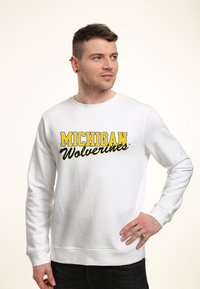 Bílý svetr s nápisem "MICHIGAN" v tučně žluté barvě a "Wolverines" v černém písmu. Hladké manžety a spodní lem, jemná textilie.