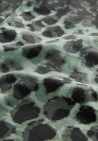 Mønstret stof i nuancer af grøn og sort med et leopardprint-design, der har varierede former og teksturer. Glat tekstiloverflade.