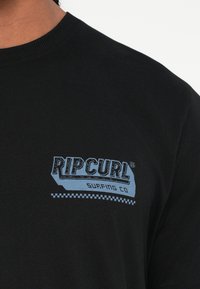 Crna pamučna majica s plavim grafičkim otiskom na kojem piše "RIPCURL" i "SURFING CO", rebrastim izrezom i kariranim detaljima.