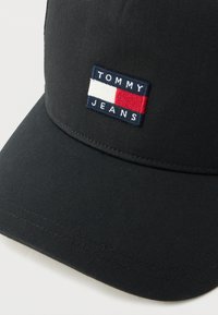 Črna bejzbol kapa z vezenim pravokotnim logotipom Tommy Jeans v mornarsko modri, beli in rdeči barvi, ki je centriran na sprednjem delu.