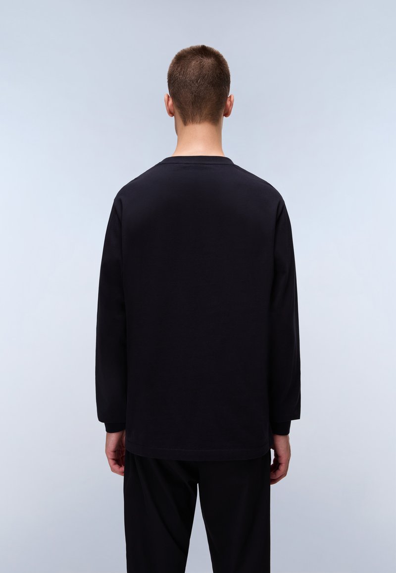 T-shirt lungo nero a maniche lunghe con scollo rotondo, texture liscia e vestibilità rilassata. Mostrato su una persona vista di spalle.