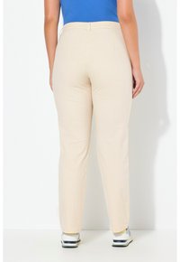 Beige stretchbroek met een rechte pijp en tailleband, met een zachte textuur en een effen ontwerp, gecombineerd met witte en grijze sneakers.