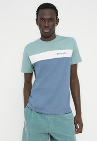 Κοντομάνικο μπλουζάκι σε ανοιχτό μπλε, σκούρο μπλε και λευκό. Διαθέτει το λογότυπο "RIPCURL" στο στήθος, στρογγυλή λαιμόκοψη και μαλακό ύφασμα από βαμβακερό μείγμα.