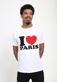 Bílá bavlněná tričko s výrazným černým textem "PARIS" a symbolem červeného srdce. Krátké rukávy a střih s kulatým výstřihem.