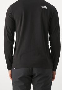 Schwarzes langärmeliges T-Shirt aus Baumwolle mit kleinem weißem Logo auf dem oberen Rücken und lockerem Schnitt. Keine auffälligen Muster oder Texturen.