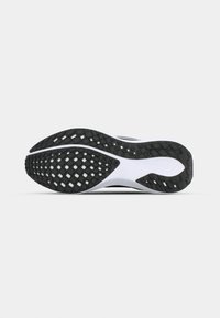Semelle de chaussure avec une bande de roulement en caoutchouc noir et blanc présentant un motif en grille pour l'adhérence, affichée sur un fond gris clair uni.