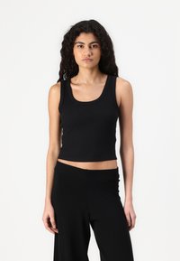 Black, fitted cropped tank top made of a smooth, stretchy fabric with a round neckline and wide shoulder straps. Paired with black pants.