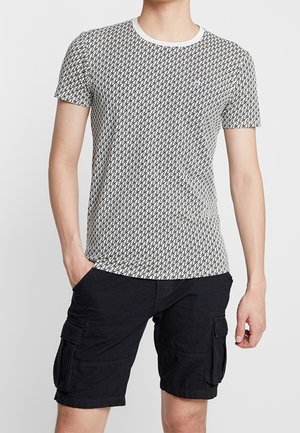 Camiseta de manga corta de algodón, con un patrón geométrico en blanco y negro, cuello redondo y corte ajustado. Combinada con pantalones cortos cargo negros.