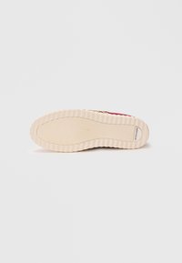 Rubber sneaker sole featuring a textured beige surface with a ribbed pattern. Includes a small brand logo near the heel.