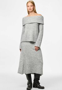 Suéter gris de punto sin hombros con cuello acanalado, combinado con una falda larga gris a juego. La modelo lleva botas negras hasta la rodilla.