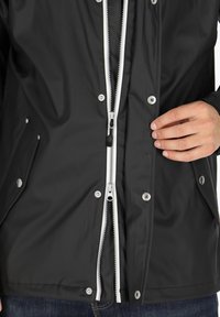 Czarna wodoodporna kurtka wyposażona w podwójny zamek błyskawiczny, srebrne zatrzaski, boczne kieszenie oraz gładką, błyszczącą fakturę materiału.