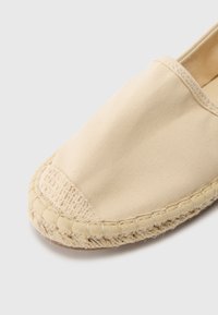 Beige canvas espadrille met een ronde neus en een gevlochten jute zool. Lichtgewicht materiaal; eenvoudig, naadloos ontwerp; textuurdetails op de neus.