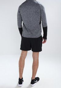 Sportoutfit mit einem taillierten, grauen Langarmshirt mit schwarzen Akzenten und schwarzen Shorts; ergänzt durch schwarze Sportschuhe.