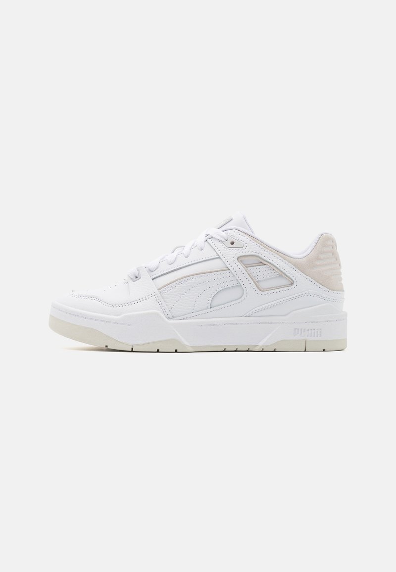 Basket basse blanche avec lacets, panneaux texturés et talon beige coussiné, vue de profil sur un fond uni.