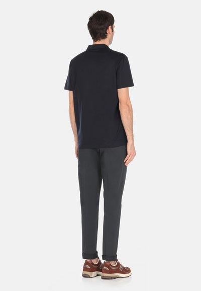 Camiseta polo navy de manga corta combinada con pantalones oscuros grises. Zapatillas marrones con acentos blancos. Vista desde atrás.