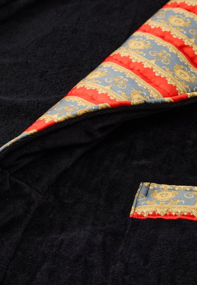 Črn beljen plašč iz frotirja, ki ima ovratnik iz vzorčaste tkanine z zlatimi, rdečimi in modrimi detajli. Vključuje tudi majhno žep z usklajenim vzorcem.