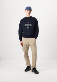 Marine sweatshirt med hvid "tommy girl" tekst, lysebeige bukser og sorte sneakers. Kappen er lyseblå med et logo på fronten.