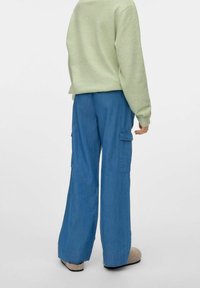 Sudadera verde claro, pantalones cargo azules con bolsillos laterales, diseño de pierna ancha, textura suave, combinados con zapatillas ligeras de color gris.