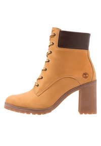 Bottine en cuir fauve avec un accent en cuir marron en haut, œillets métalliques, lacets multicolores et talon épais transparent.